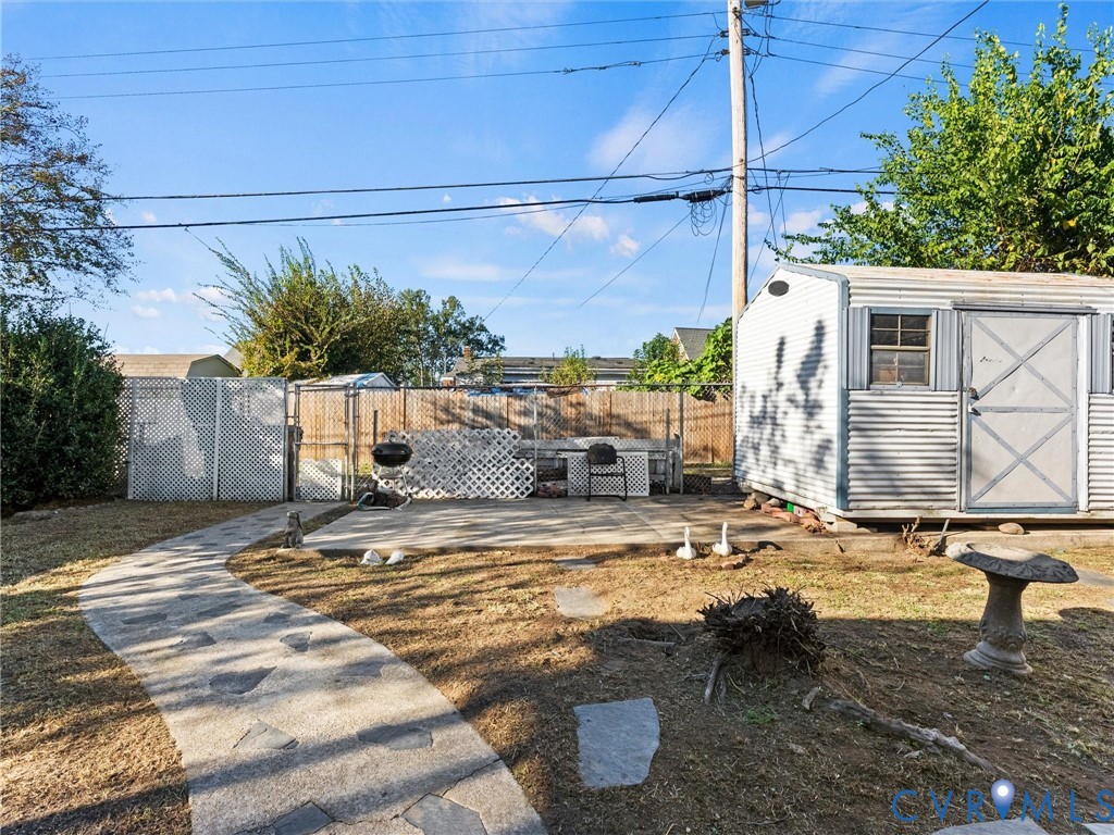 Backyard featuring a stone-paver walkway, concrete patio, storage shed with metal siding, and lattice privacy fencing