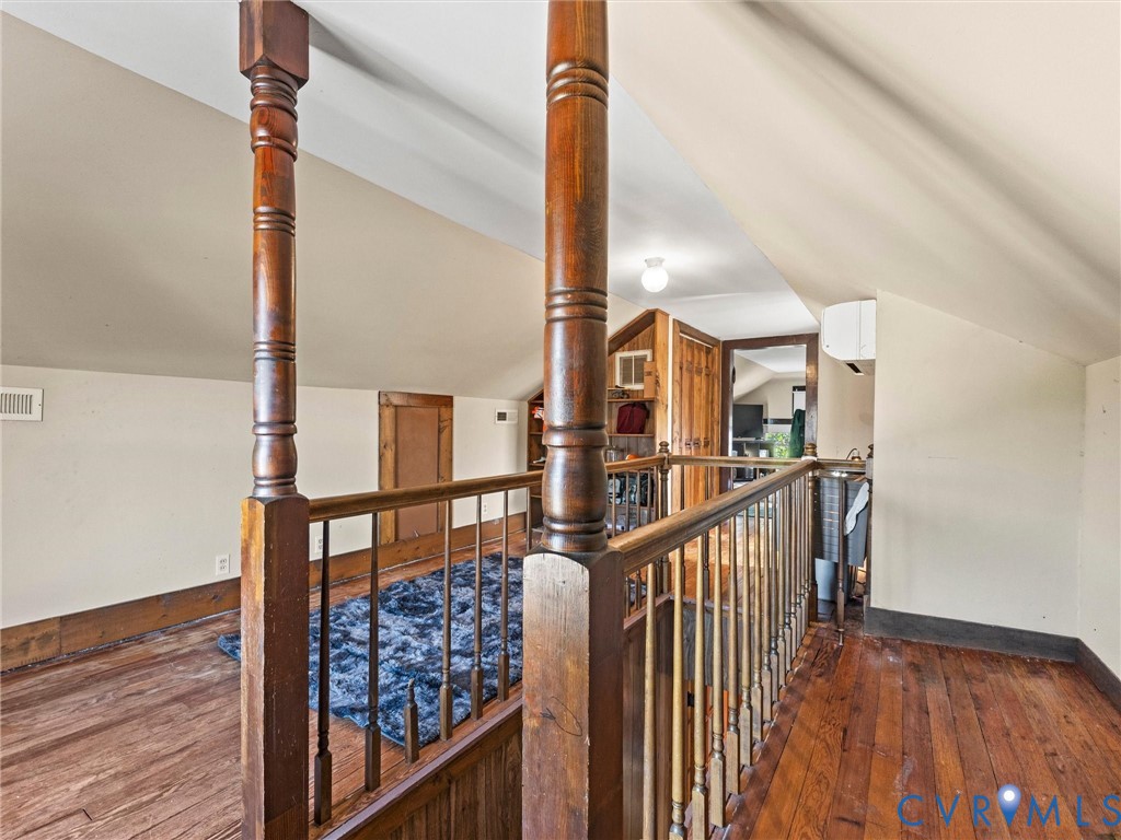 Upper level area featuring wood flooring, vaulted ceilings, and a handcrafted wooden balustrade with detailed newel posts