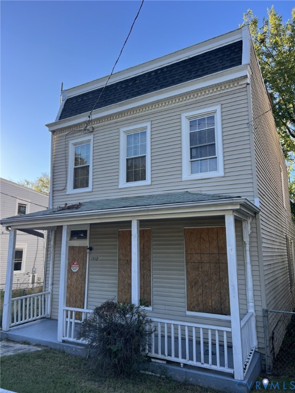 Two-story exterior featuring light-toned horizontal siding, a mansard-style roofline with decorative trim, and a covered front porch with a white wooden railing Two-story exterior featuring light-toned horizontal siding, a mansard-style roofline with decorative trim, and a covered front porch with a white wooden railing