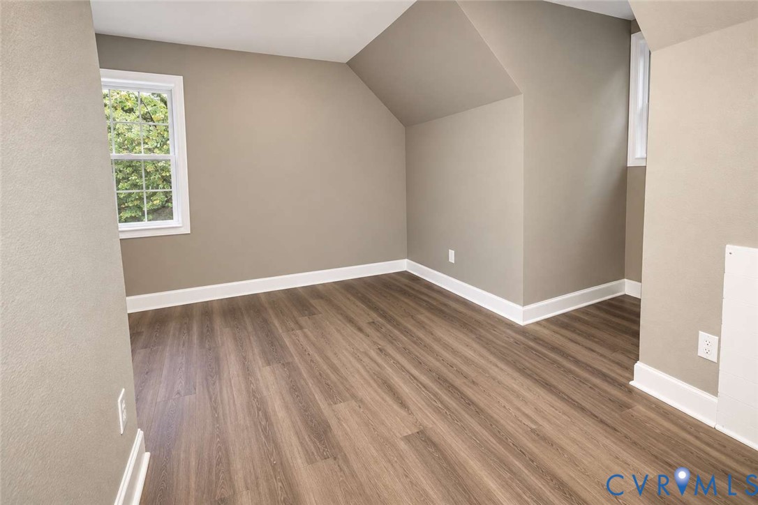 Room featuring wood-finish flooring, neutral wall paint, and multi-pane windows with architectural angled ceiling detail