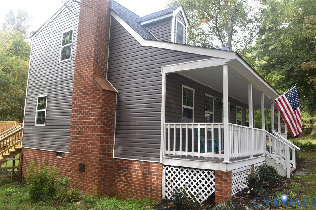 Two-story exterior featuring dark horizontal siding, a classic brick chimney, a covered front porch with white railing, and decorative lattice skirting