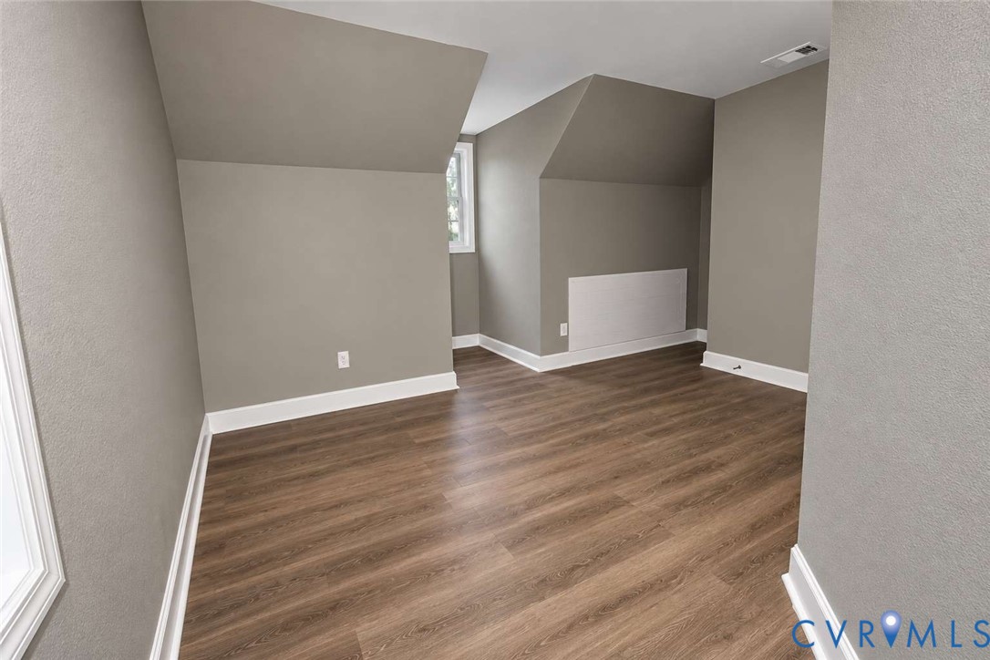 Neutral-toned room featuring sloped ceilings, wood-finish flooring, and white window trim