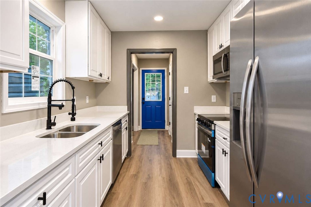 Kitchen featuring white cabinetry, solid-surface countertops, wood-finish flooring, a stainless steel refrigerator, and a matte black gooseneck faucet