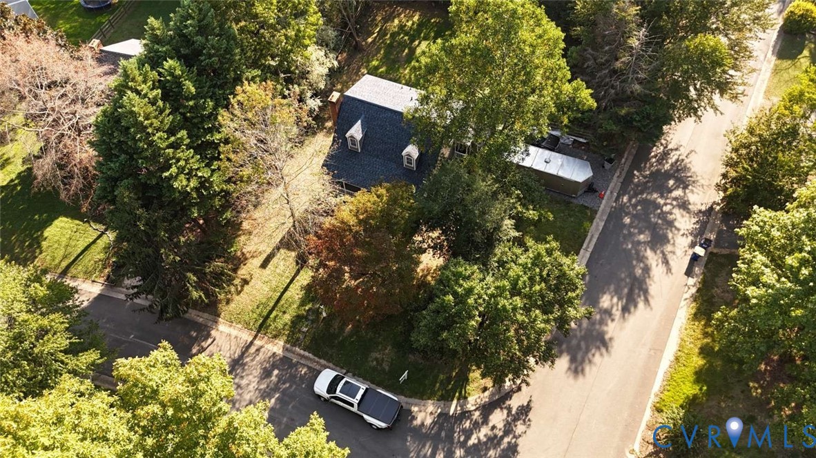 Corner lot featuring a gambrel roofline with dormer windows, surrounded by mature trees on a landscaped parcel