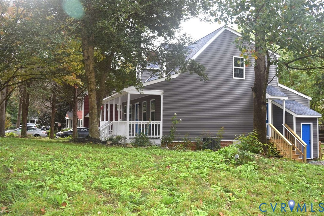 Two-story residence featuring horizontal gray siding, a covered front porch with white railing, and exterior wooden staircases