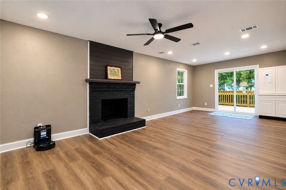 Living area featuring wood-finish flooring, a floor-to-ceiling brick fireplace with wood-paneled accent detail, recessed lighting, ceiling fan, and sliding glass door with exterior deck access
