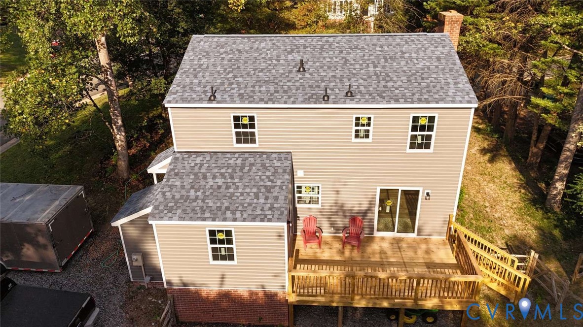 Two-story exterior featuring horizontal siding, a composite shingle roof, a brick foundation base, and a raised wooden deck with a staircase