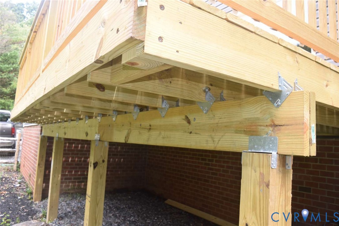 Elevated wood deck featuring structural support posts, pressure-treated lumber joists, metal joist hangers, and a red brick foundation exterior