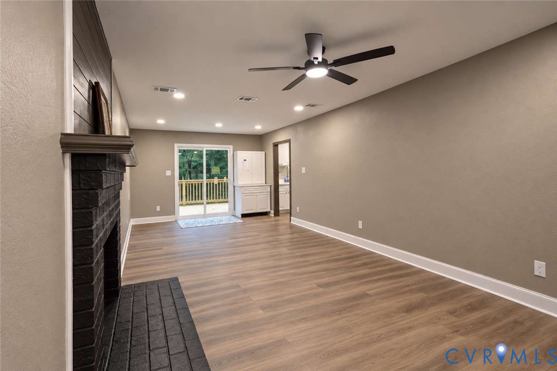 Painted brick fireplace with a wood mantle, wood-finish flooring, recessed lighting, ceiling fan with integrated light fixture, and glass sliding doors