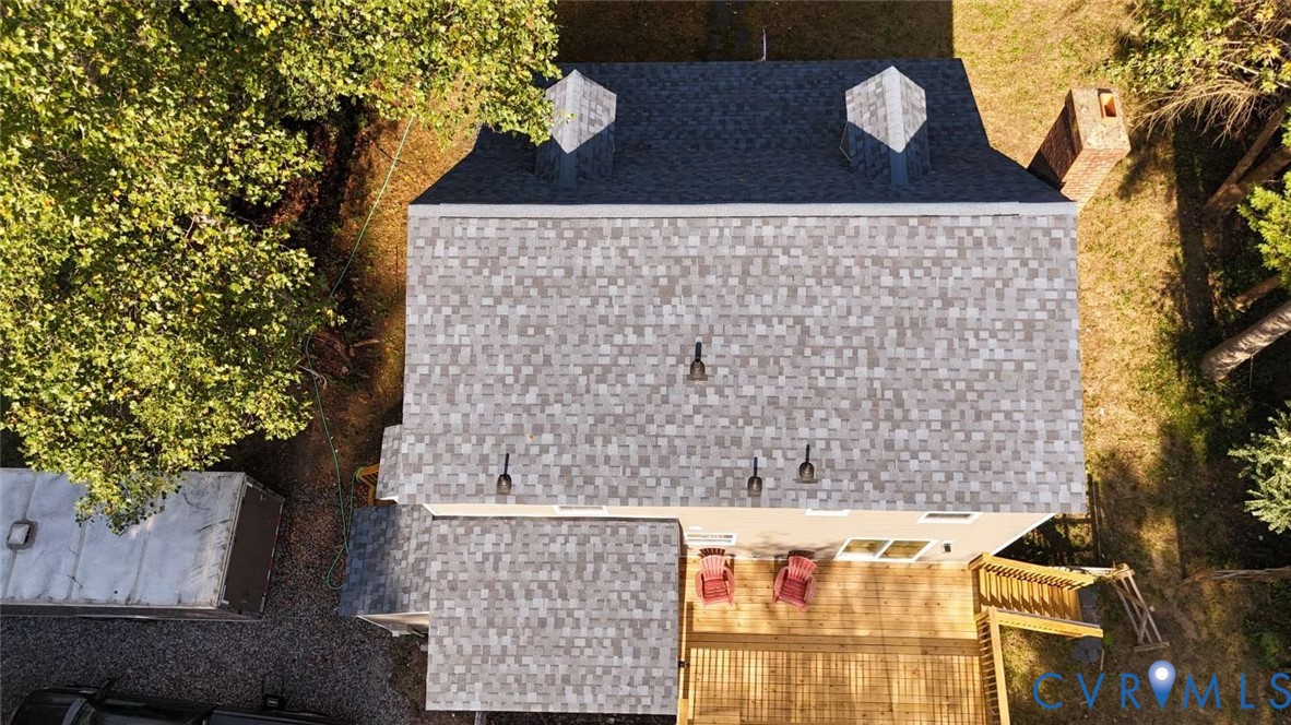Aerial perspective featuring a multi-pitched shingle roof with two dormers, a masonry chimney, and a wooden deck