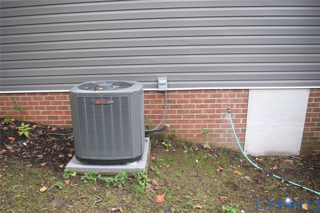 Exterior wall featuring grey horizontal siding over a red brick foundation, equipped with a central air conditioning unit and an outdoor water spigot