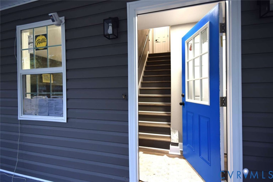 Exterior featuring dark horizontal siding, a blue paneled door with a six-pane window insert, and a single-hung window with a grid pattern