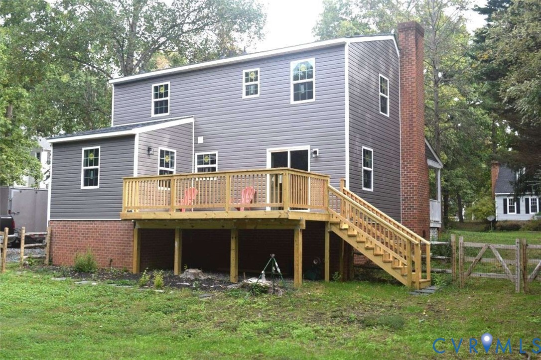 Two-story residence featuring gray horizontal siding, an exterior red brick chimney, a wood deck with staircase, and a brick foundation
