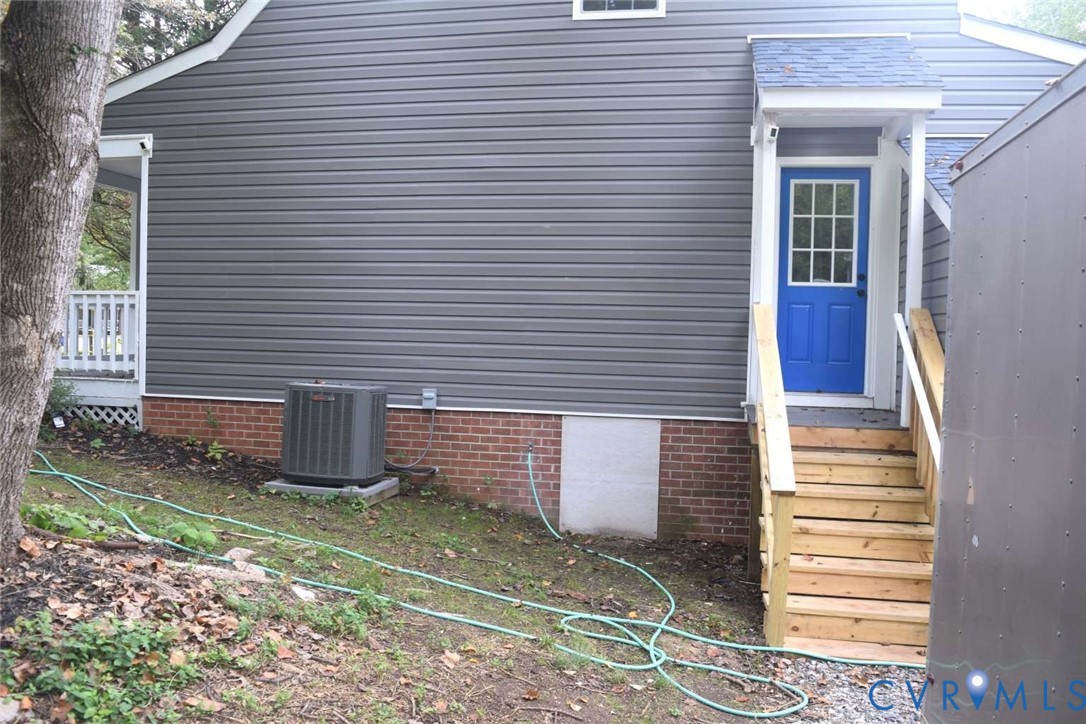 Exterior featuring dark horizontal siding, a red brick foundation, an elevated wood staircase with handrails, and a multi-pane glass entry door