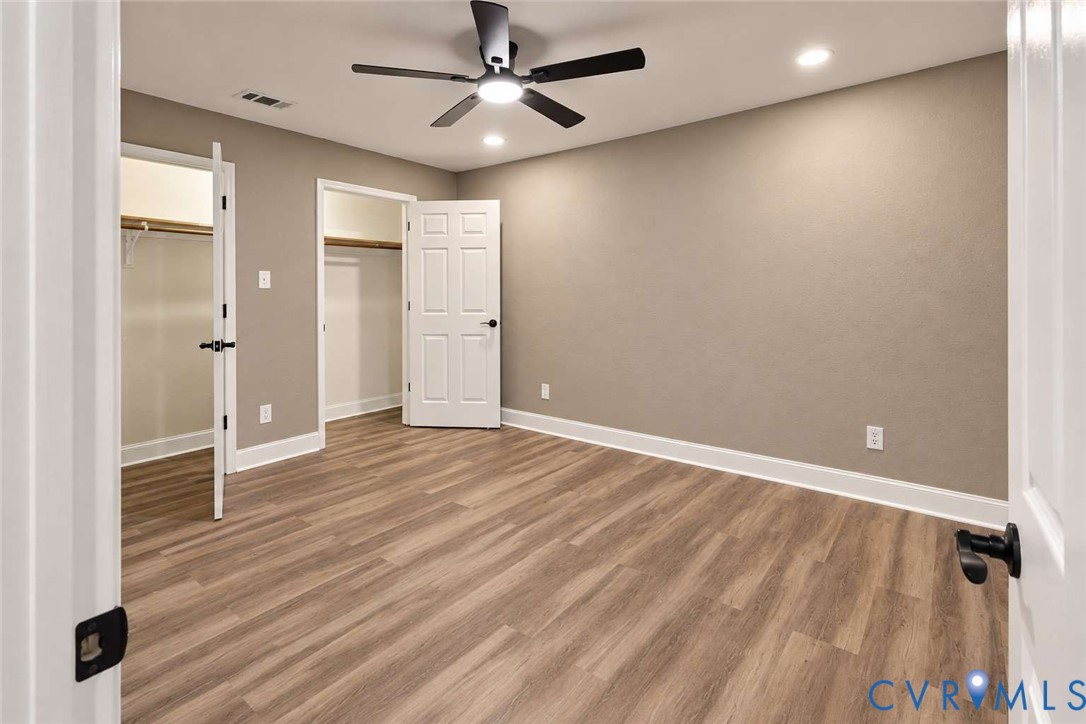 Wood-finish flooring, neutral wall tones, multi-panel doors with matte black hardware, and a center ceiling fan with integrated lighting