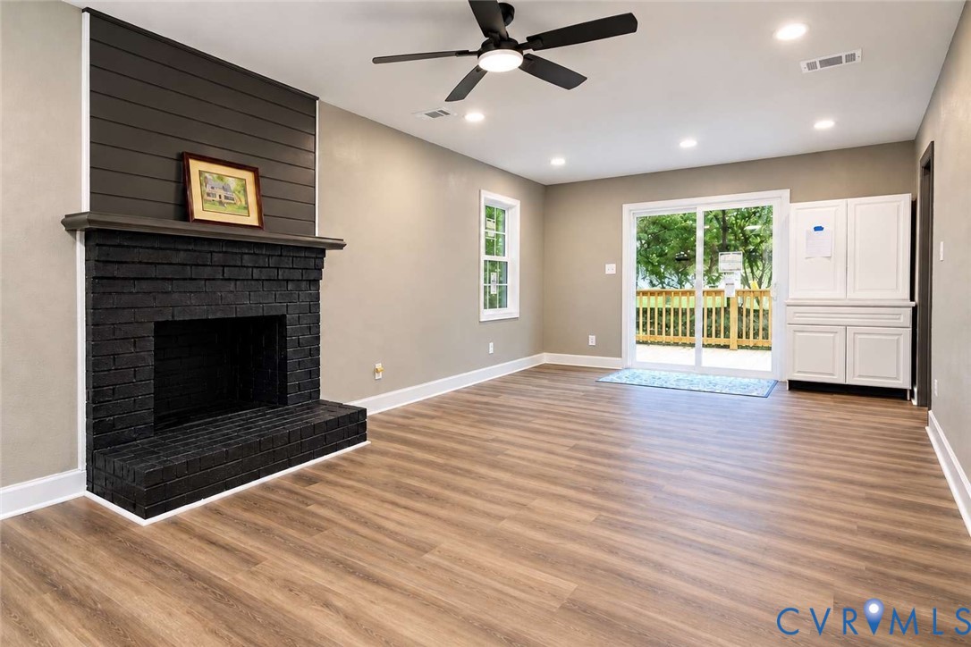 Painted brick fireplace with a horizontal shiplap accent wall, wood-finish flooring, recessed lighting, ceiling fan, and white built-in cabinetry