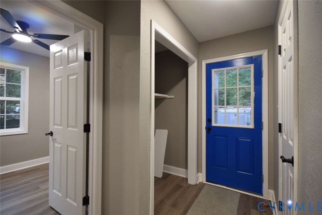 Entryway featuring a blue exterior door with a multi-pane glass insert, wood-finish flooring, white panel doors, and a ceiling fan with integrated lighting