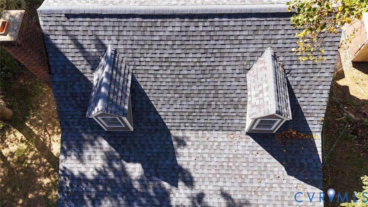 Asphalt shingle roof featuring two gabled dormers and a brick chimney