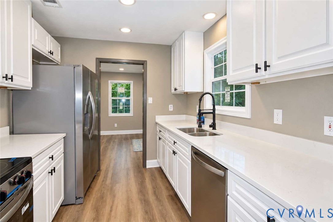 Kitchen featuring white cabinetry with matte black hardware, stone-finish countertops, stainless steel appliances, a double-basin undermount sink with a gooseneck faucet, and wood-finish flooring