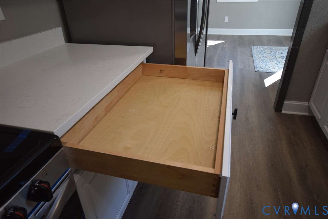 Dovetail joinery drawer construction featuring a natural wood-finish interior and smooth-gliding tracks, paired with white cabinetry, light-toned stone-surface countertop, and wood-finish flooring