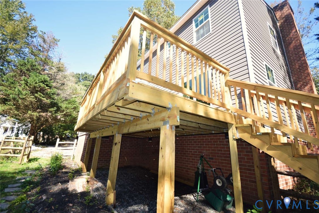 Elevated wooden deck featuring railing, staircase, and support posts, set against a two-story exterior with brick foundation and horizontal siding