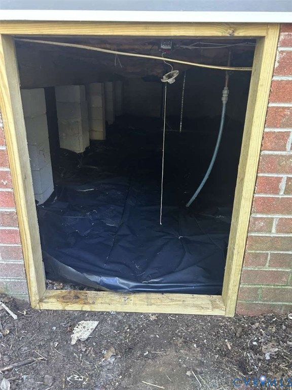 Crawl space featuring concrete block piers, a moisture barrier foundation cover, brick exterior siding, and treated wood framing
