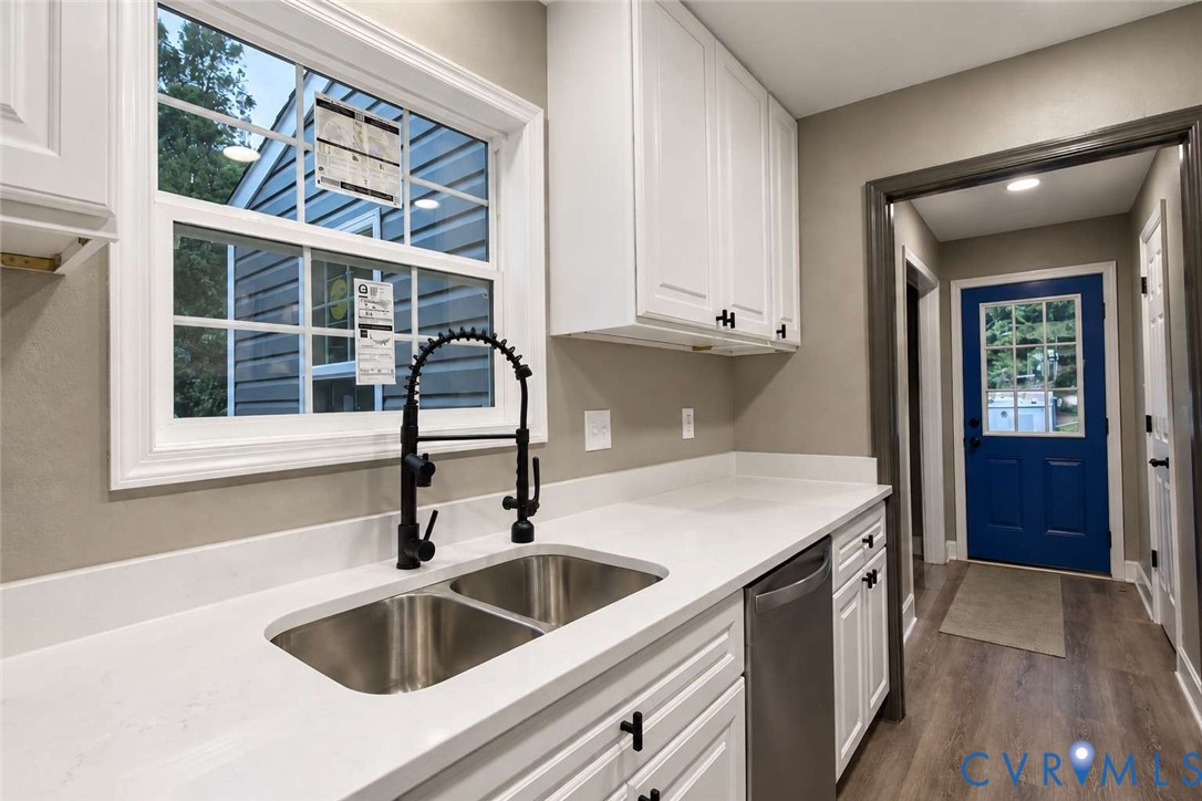 Kitchen featuring white shaker-style cabinetry, solid-surface countertops, dual-basin stainless steel sink with matte black gooseneck faucet, and stainless steel dishwasher