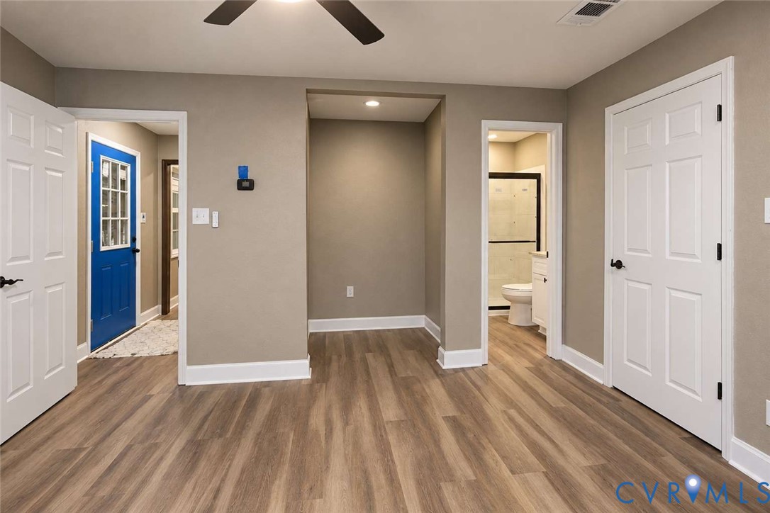 Neutral-toned interior featuring wood-finish flooring, a recessed ceiling fan, multiple six-panel interior doors, and a blue exterior door with glass panes