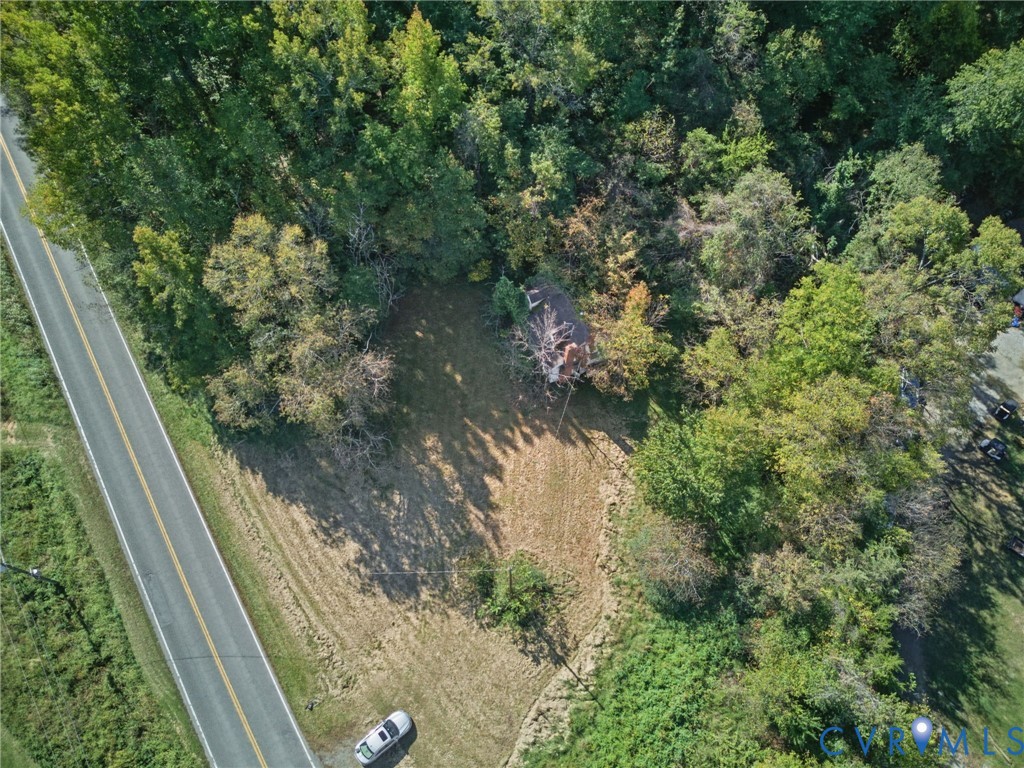 Aerial perspective featuring a wooded lot with cleared grass area and frontage on a paved road