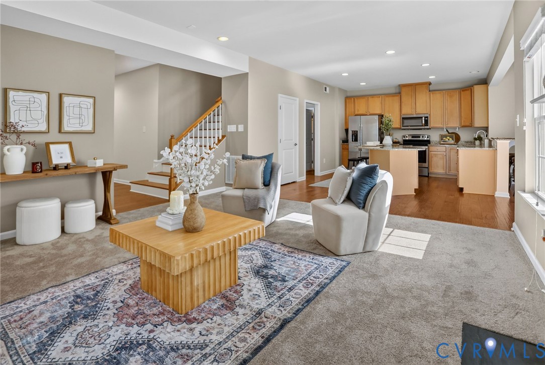 Open-concept interior featuring wood-finish flooring, a kitchen with natural wood cabinetry and a central island, recessed lighting, and a staircase with a wooden handrail