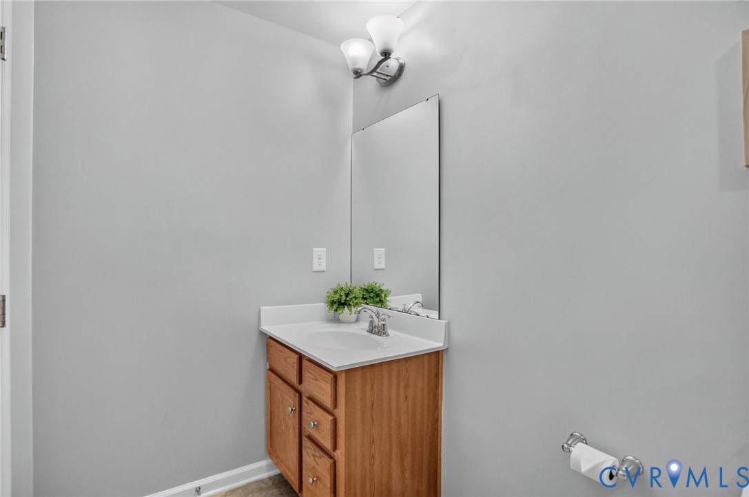 Single-sink vanity with wood-finish cabinetry, solid-surface countertop, integrated basin, wall-mounted mirror, and dual-bulb fixture