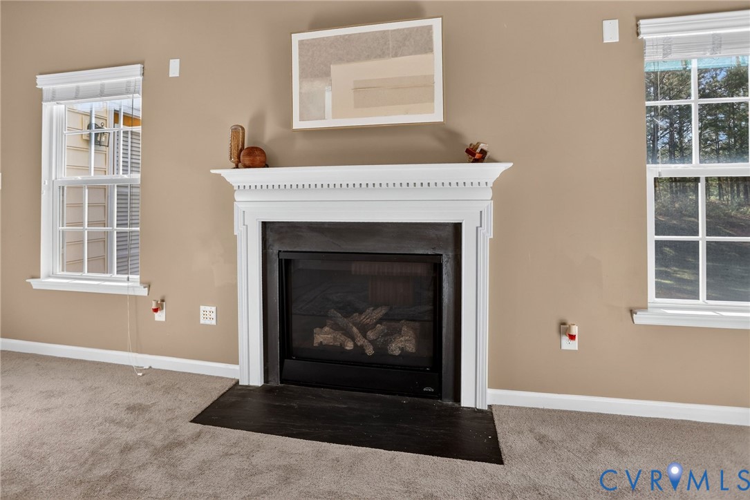 Fireplace with a classic white decorative mantel, dark tile surround, and black hearth, framed by dual windows with integrated blinds