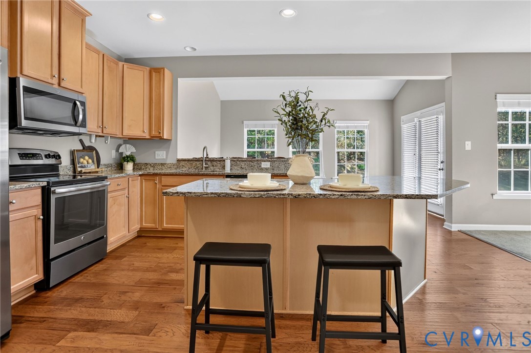 Kitchen featuring natural wood cabinetry, stone-finish countertops, stainless steel appliances, a central island, and wood-finish flooring