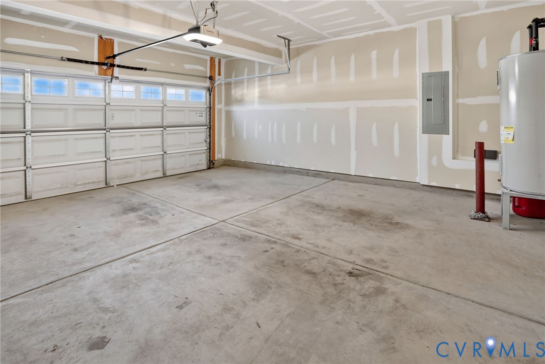 Attached two-car garage featuring a sectional door with windows, concrete flooring, and a wall-mounted water heater