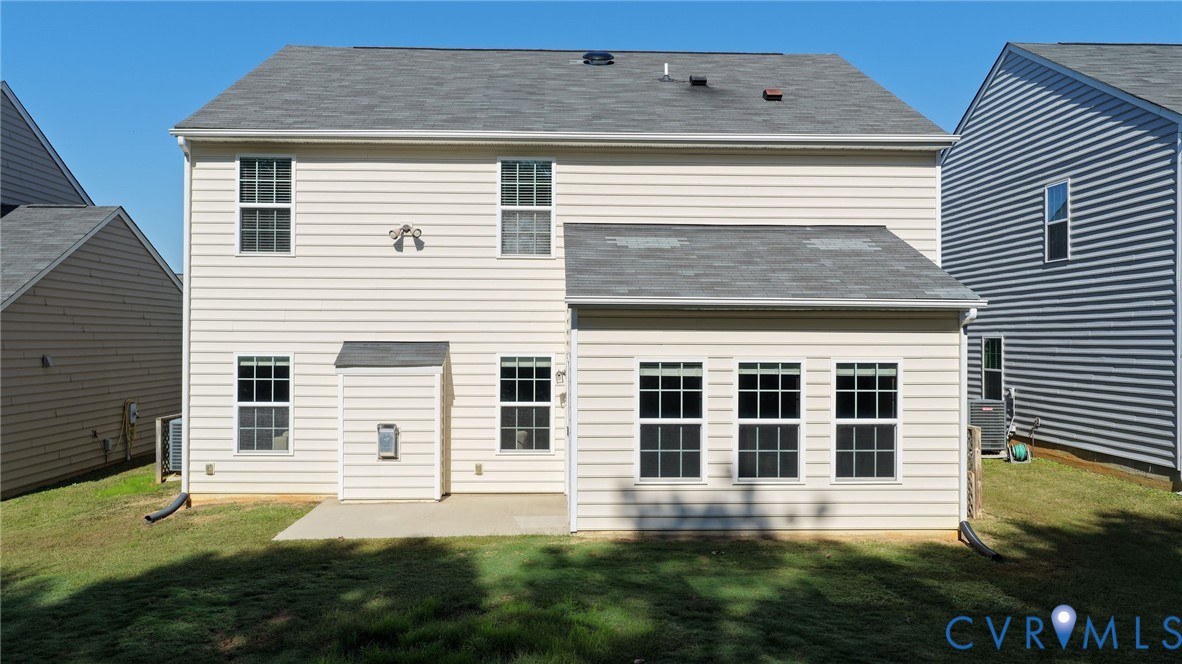 Rear exterior featuring light-toned horizontal siding, a composite shingle roof, multiple grid-pattern windows, and a concrete patio