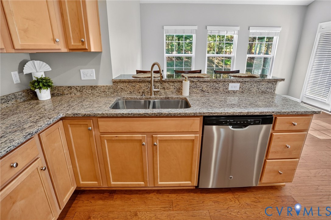 Kitchen featuring natural wood cabinetry, stone-surface countertops, stainless steel dishwasher, double-basin undermount sink, and multi-pane windows
