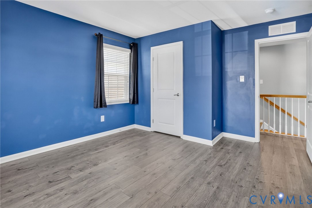 Room featuring wood-finish flooring, a single-panel interior door, and a multi-pane window with a horizontal blind