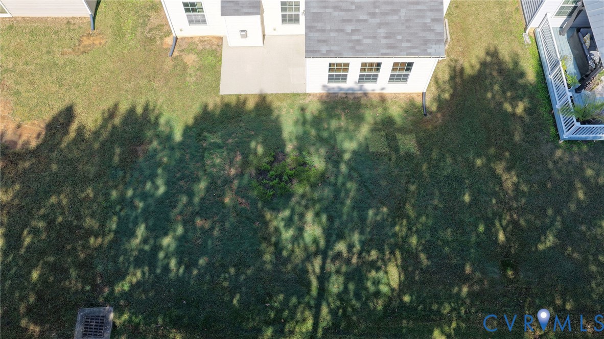 Aerial perspective of a rear yard featuring a concrete patio, light-toned exterior siding, and a gabled roofline