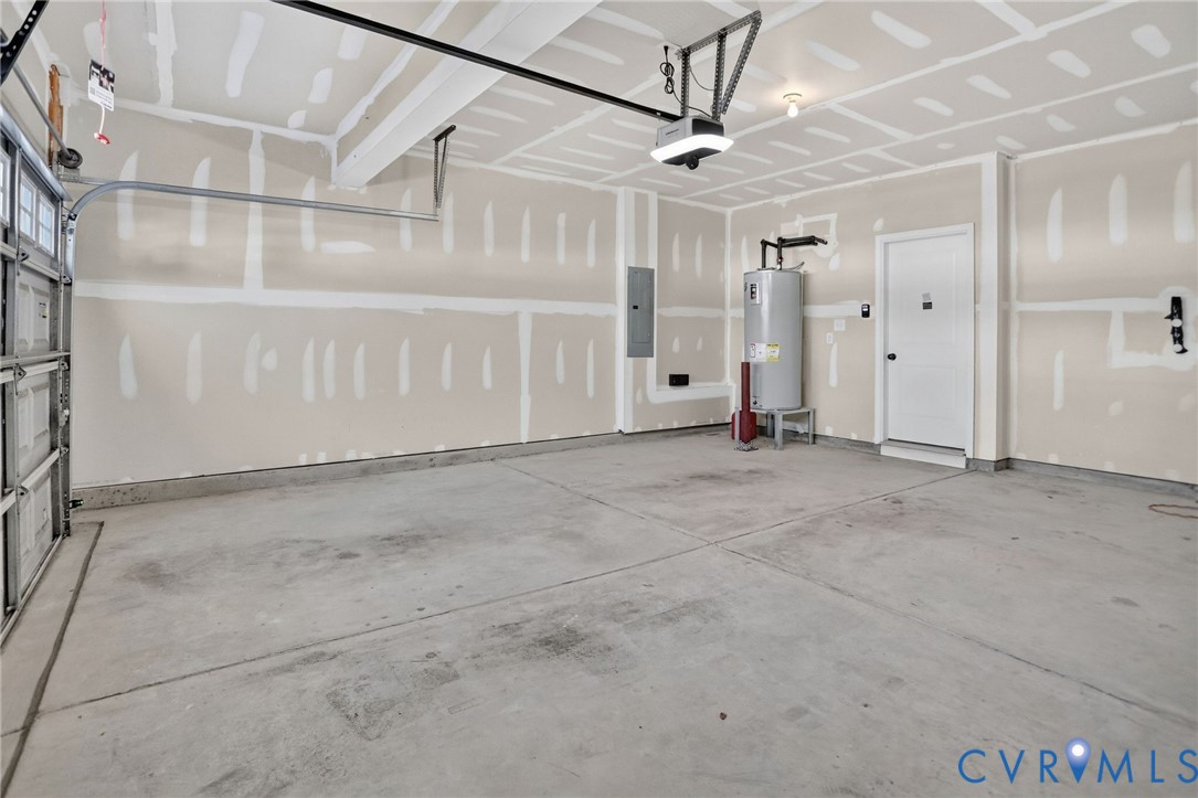 Attached garage featuring concrete flooring, drywall finish, a dedicated water heater, and an automatic door opener