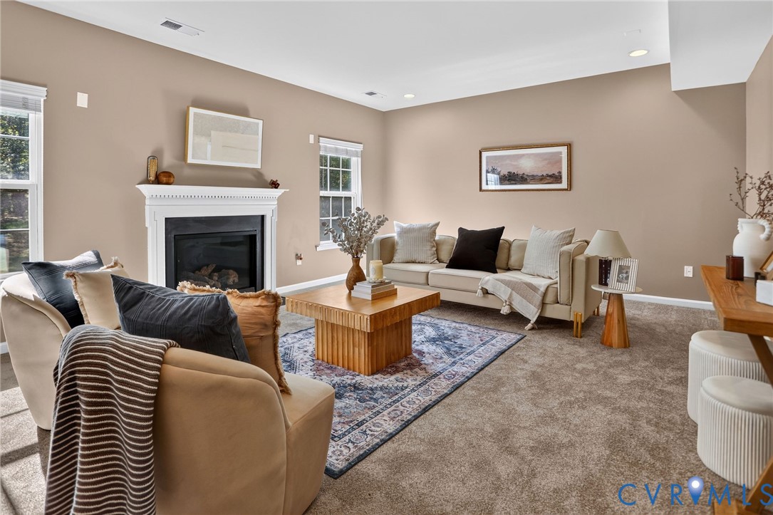 Living area featuring a fireplace with a white mantel surround, carpeted flooring, recessed lighting, and windows with blinds Living area featuring a fireplace with a white mantel surround, carpeted flooring, recessed lighting, and windows with blinds