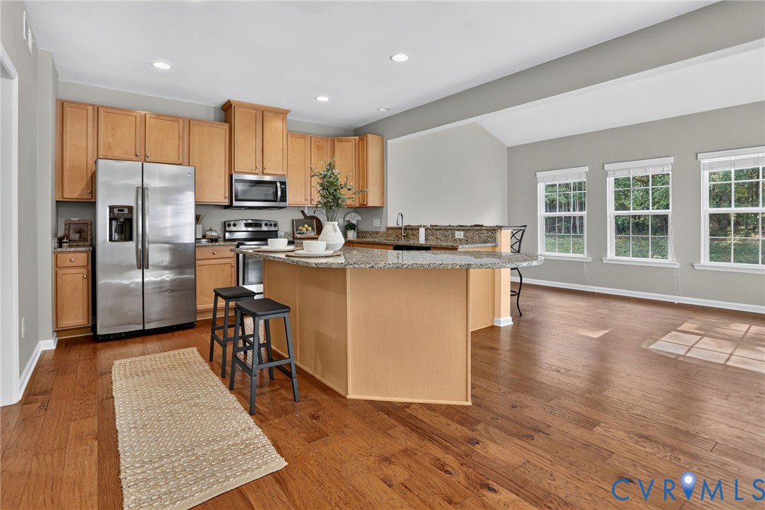 Kitchen featuring wood-finish cabinetry, stone-surface countertops, center island, stainless steel appliances, and hardwood flooring