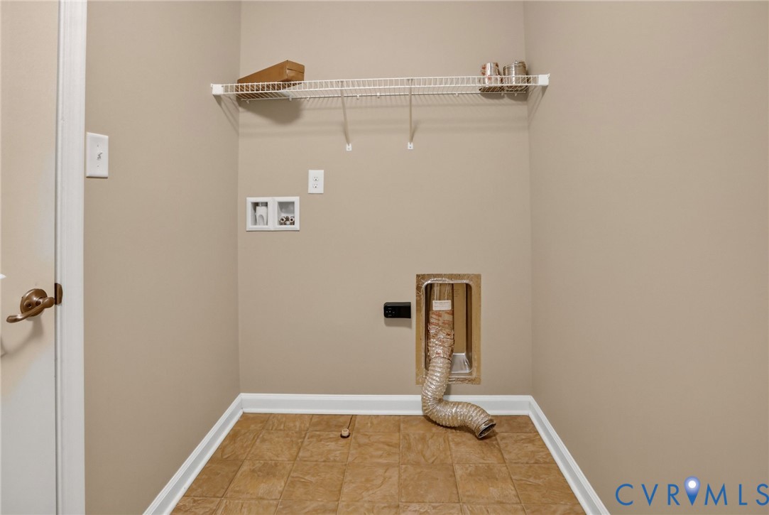 Laundry area featuring tile flooring, a wall-mounted wire storage shelf, and dedicated water and dryer vent hookups