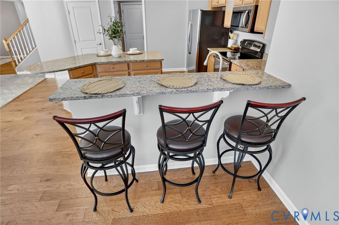 Kitchen featuring a tiered stone-surface peninsula, light wood-finish cabinetry, built-in stainless steel appliances, and wood-finish flooring