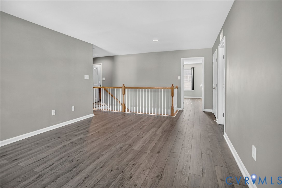 Open area featuring wood-finish flooring, neutral wall paint, and a staircase with a wooden handrail and white balusters