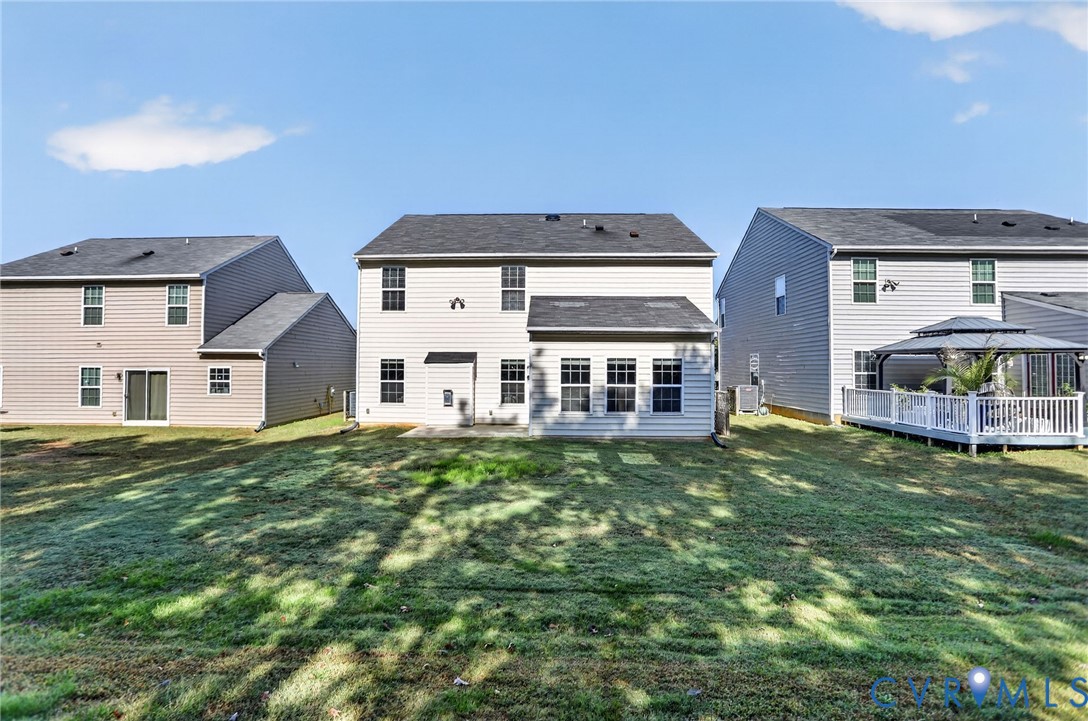 Rear exterior elevation featuring vinyl siding, multi-pane windows, a dark shingled roof, and an open backyard