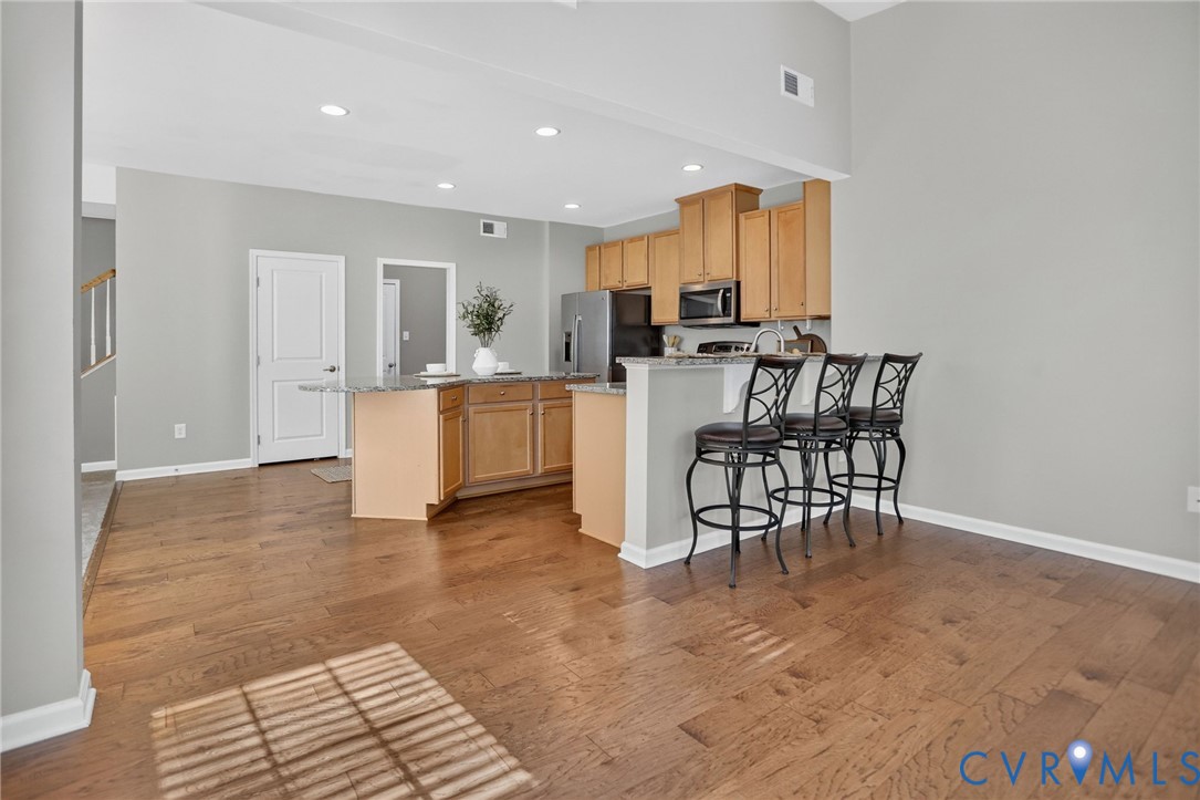 Kitchen featuring wood-finish flooring, wood cabinetry, stone countertops, an island, and recessed lighting