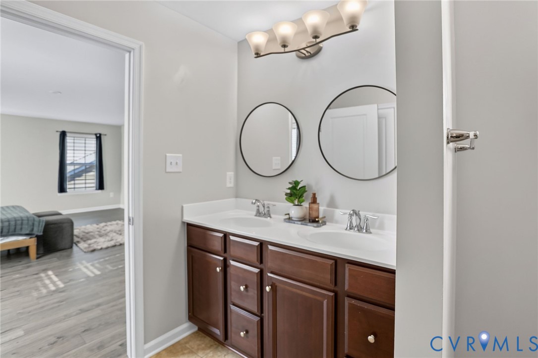Double vanity featuring wood cabinetry, white countertops with dual integrated sinks, chrome fixtures, and circular wall-mounted mirrors