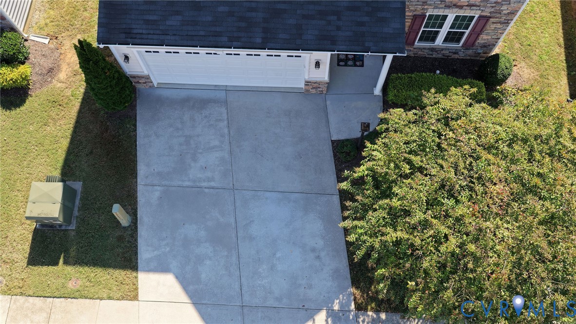 Aerial perspective of a two-car garage with a concrete driveway, stone veneer facade, shingled roof, and manicured landscaping