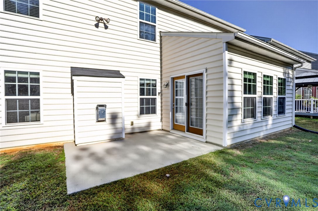 Exterior rear elevation featuring light-colored horizontal siding, a paved concrete patio, and a multi-pane sliding glass door