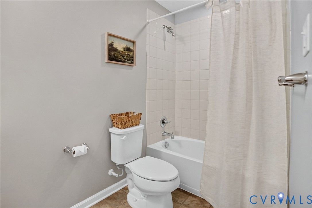 Full bathroom featuring a white porcelain tub, ceramic tile wall surround, chrome shower fixtures, and a white elongated toilet